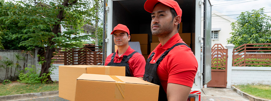Two men dressed in red shirts and hats transport boxes during a move in Eagle, ID, featured in a neighborhood guide.