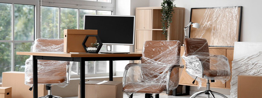 A room filled with boxes and furniture, all covered in plastic, indicating preparation for relocation.