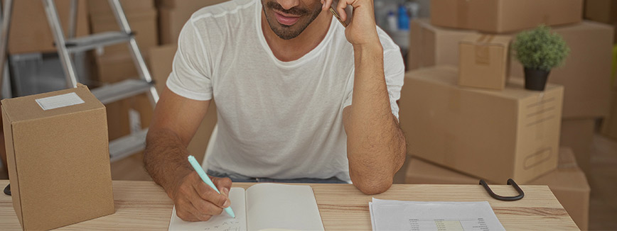 A man sits at a desk surrounded by boxes, preparing for a move with efficient storage solutions for a smooth transition.