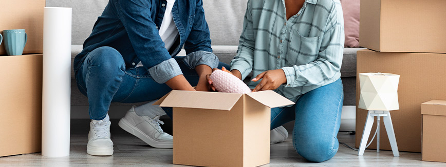 Two individuals seated on the floor with various boxes around them, indicating a local move in Kuna.