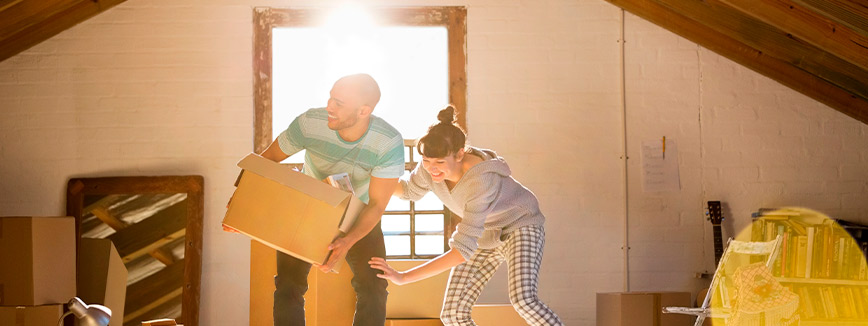 A couple is seen moving boxes in an attic, illustrating the decluttering process for residents preparing to move in Idaho.