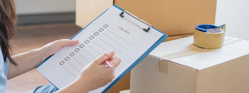 A woman holds a coffee cup and writes on a clipboard, planning winter-proofing strategies for her basement remodeling.