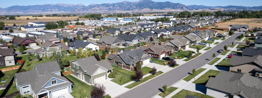 Aerial view of a suburban neighborhood with modern homes, streets, and mountain views in Bozeman, Montana on a clear day.